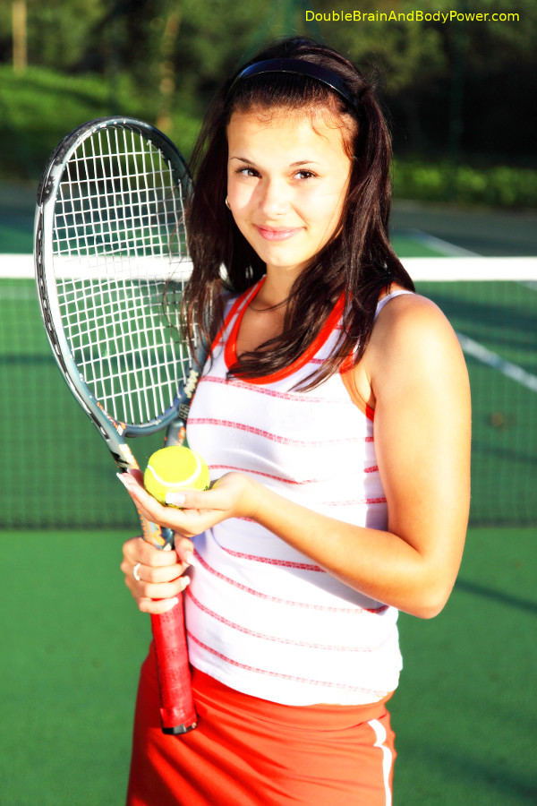 Picture of a lovely brunette lady on a tennis court holding a tennis ball in one hand and a tennis racket in the other. She is wearing a white tank top with red horizontal stripes and red shorts.