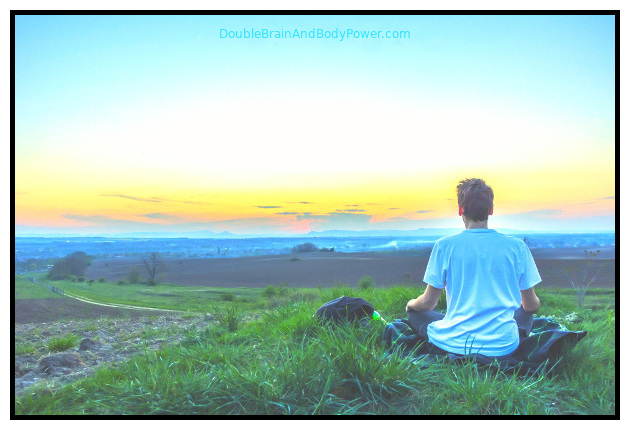 Image of a man meditating while sitting on a green grassy area with the blue ocean and waves in the distance.