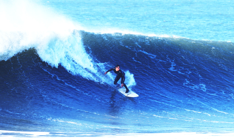 Man in black wet suit surfing on large blue wave at Croyde Bay, Croyde, UK
