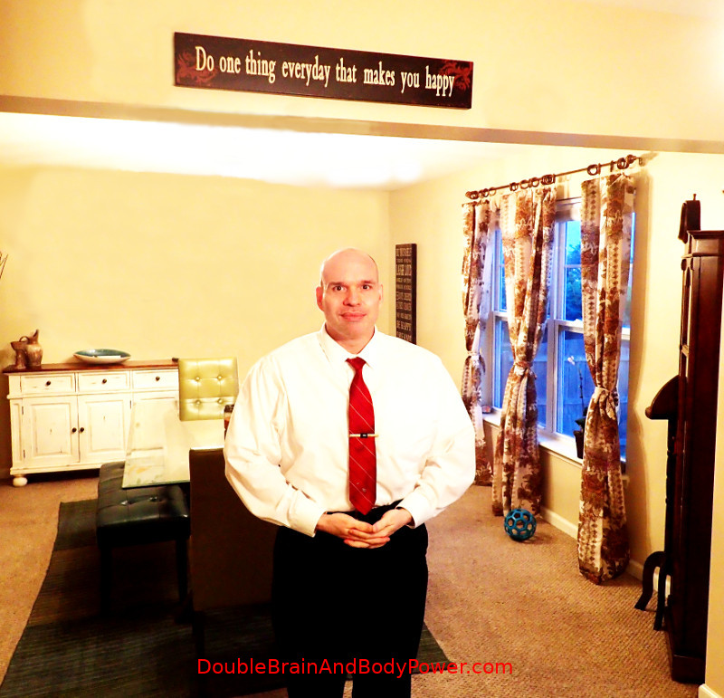 Mark in a white shirt and red tie standing in a nice beige colored room. A wood sign above says,